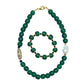 A hunter green beaded necklace with a brass focal bead and a baroque pearl, featuring hematite spacers and lampwork glass beads with matching bracelet against white background.