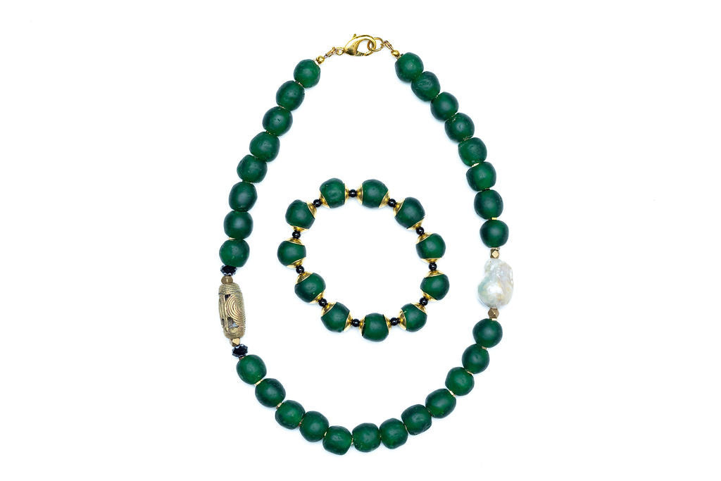 A hunter green beaded necklace with a brass focal bead and a baroque pearl, featuring hematite spacers and lampwork glass beads with matching bracelet against white background.