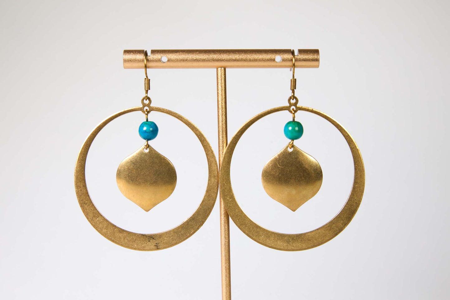 Gold hoop earrings with turquoise beads on a gold stand against a white background