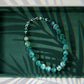 Green beaded bracelet on a dark green tray with leaf shadows