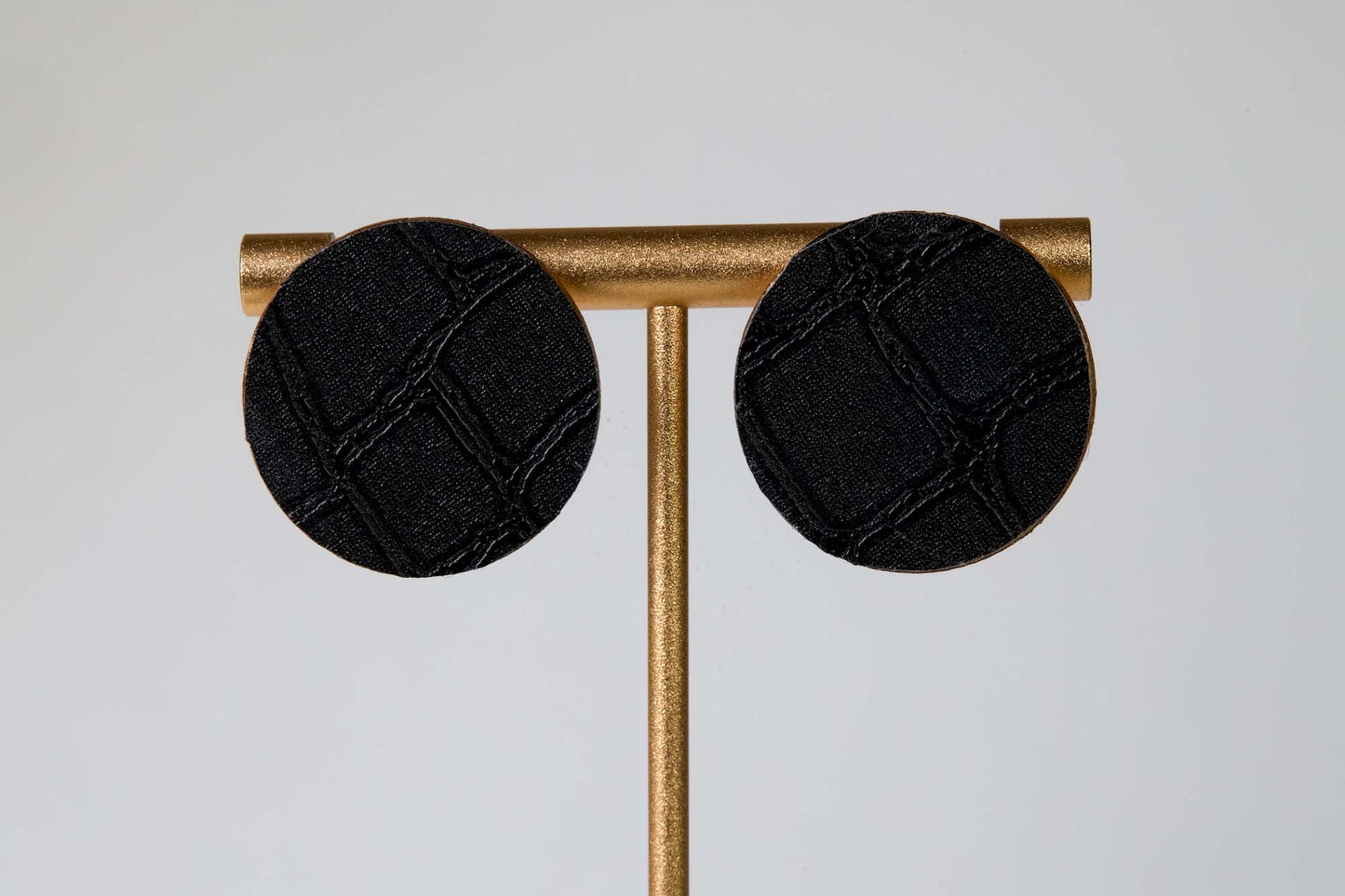 Black round earrings on a gold stand against a light gray background