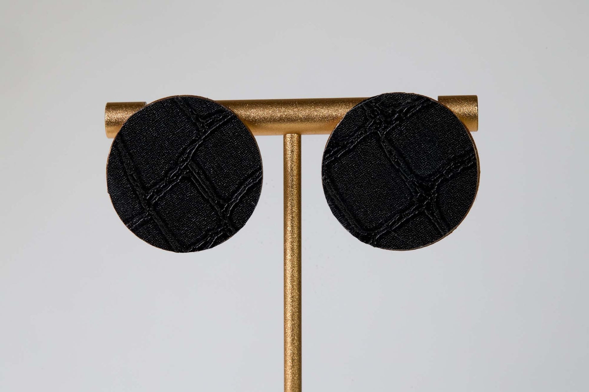 Black round earrings on a gold stand against a light gray background