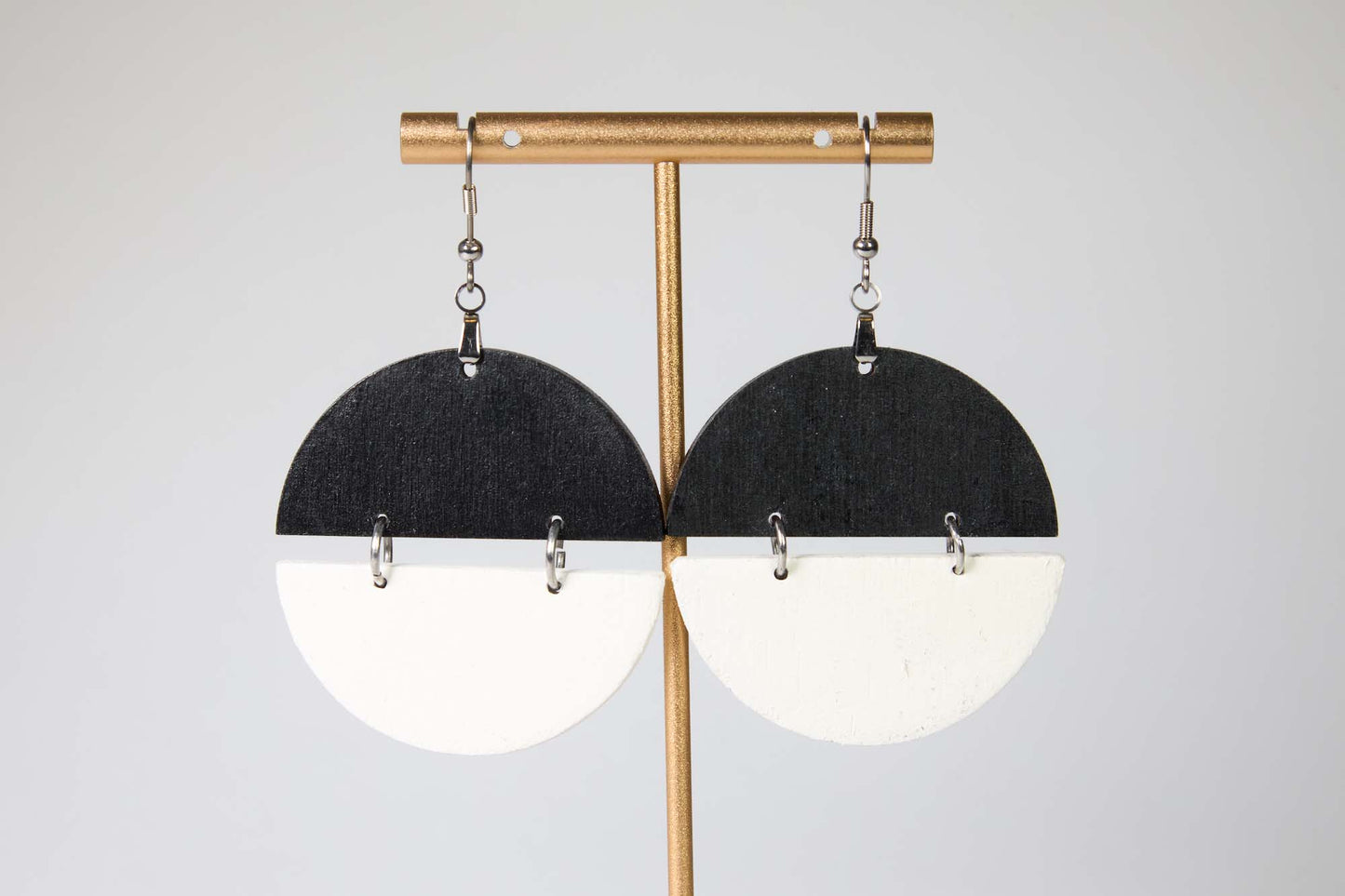 Pair of earrings with black and white half-circle design on a gold stand against a light gray background
