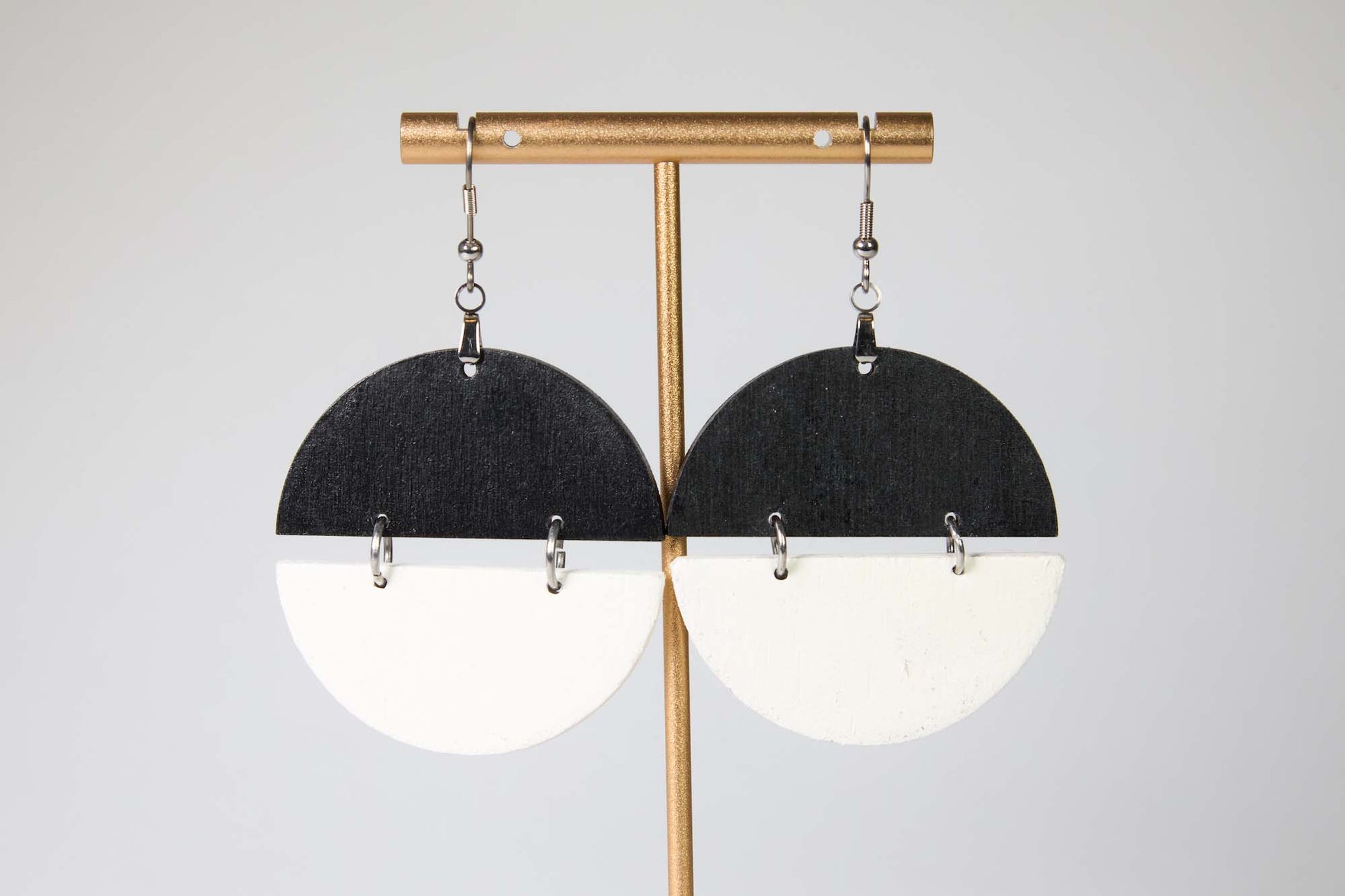 Pair of earrings with black and white half-circle design on a gold stand against a light gray background
