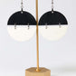 Gold earring stand with black and white half-circle earrings on a white background