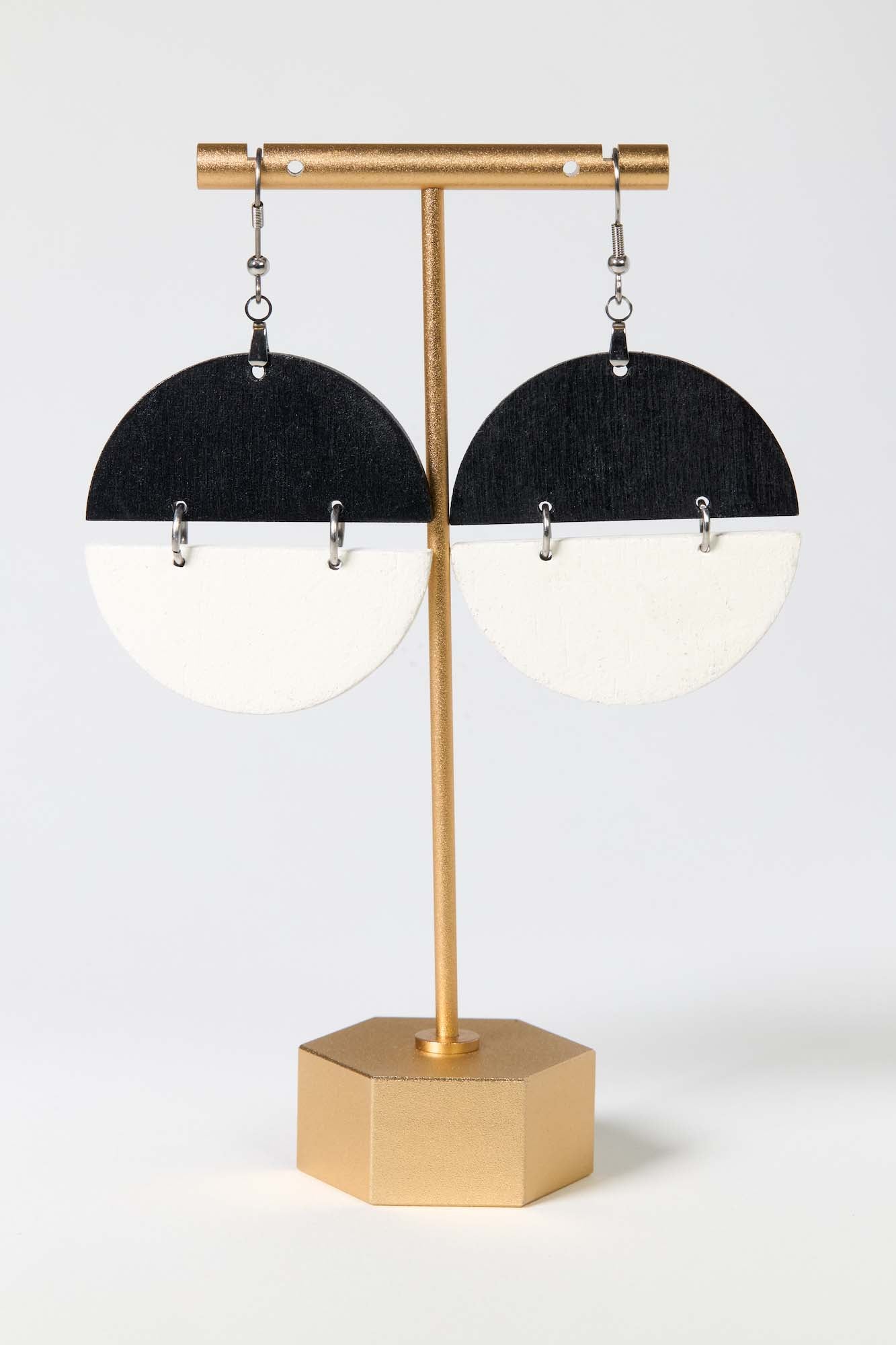 Gold earring stand with black and white half-circle earrings on a white background