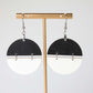 Black and white half-circle earrings on a gold earring stand against a white background