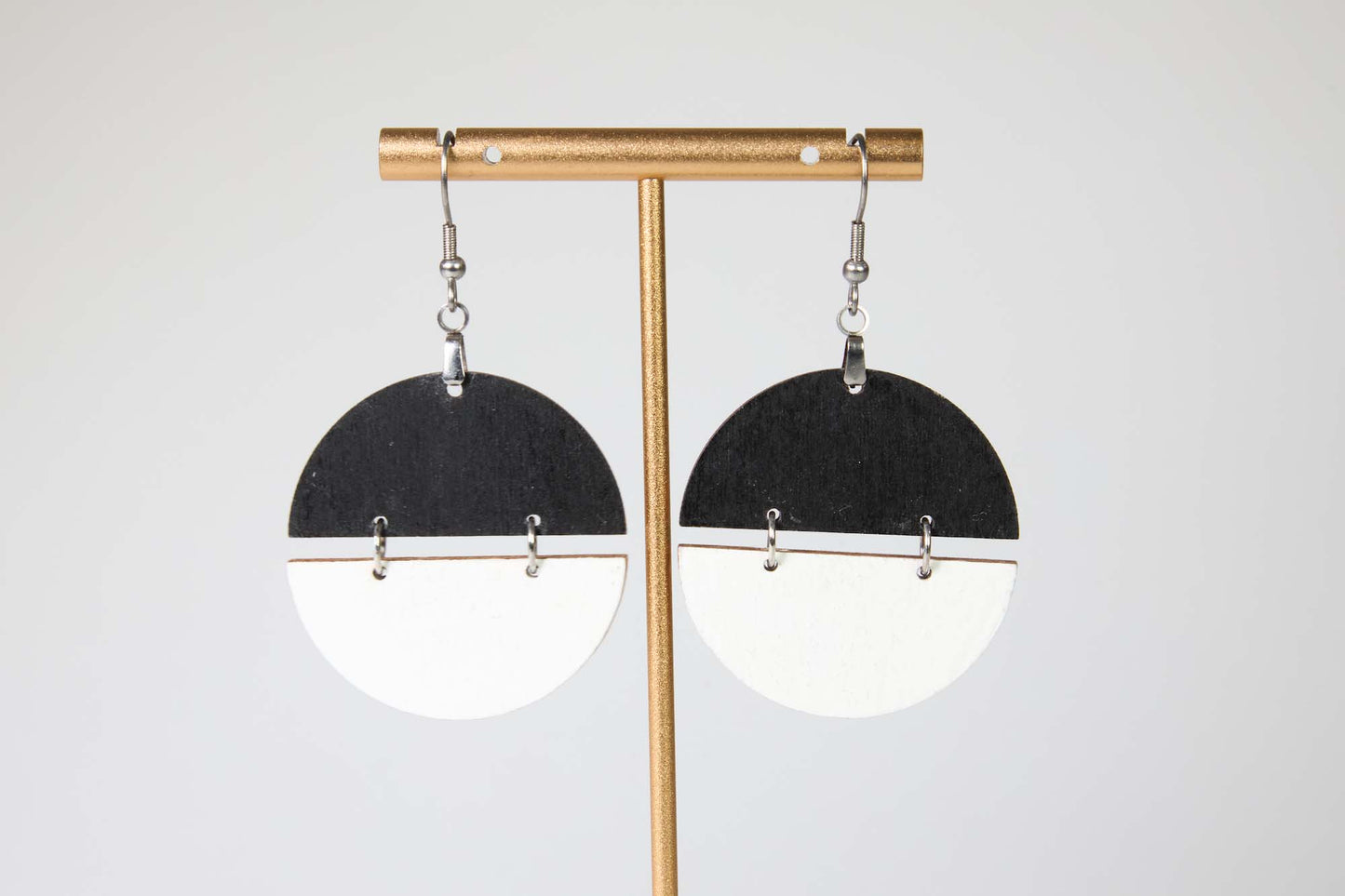 Black and white half-circle earrings on a gold earring stand against a white background