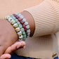 Person wearing a stack of colorful beaded bracelets on a blurred background