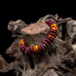 A multicolored bead bracelet with a mix of brown, orange, and yellow hues, featuring brass donut beads and fused rondelle African recycled glass beads on tree trunk against a black background.