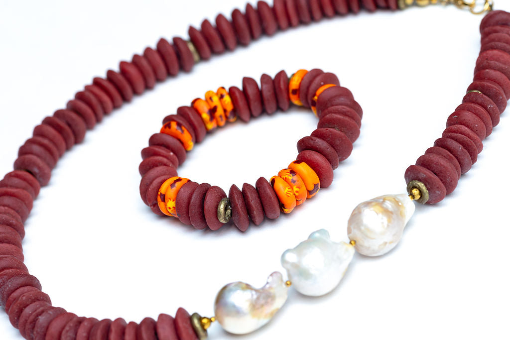 A Cicely necklace featuring a combination of burgundy Ashanti beads and freshwater baroque pearls, with brass accents and gold-plated lobster clasp, with coordinating bracelet, against white background.