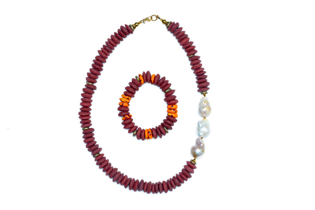 A Cicely necklace featuring a combination of burgundy Ashanti beads and freshwater baroque pearls, with brass accents and gold-plated lobster clasp, with coordinating bracelet, against white background.