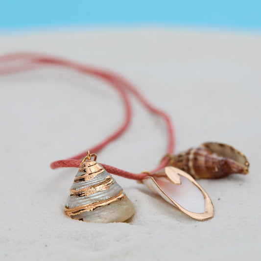 Necklace with shell pendant and pink cord on sand with blue background