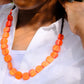 Person wearing a white top with an orange beaded necklace