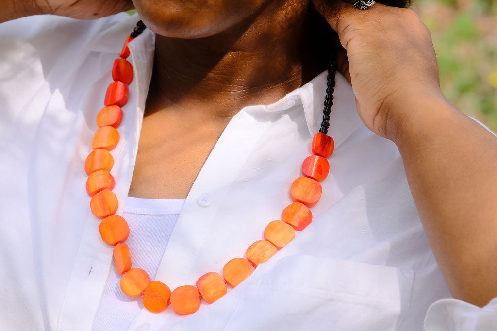 Person wearing a white top with an orange beaded necklace