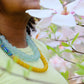 Person wearing a colorful beaded necklace with a blurred background of flowers