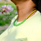 Person wearing a green necklace with a blurred floral background