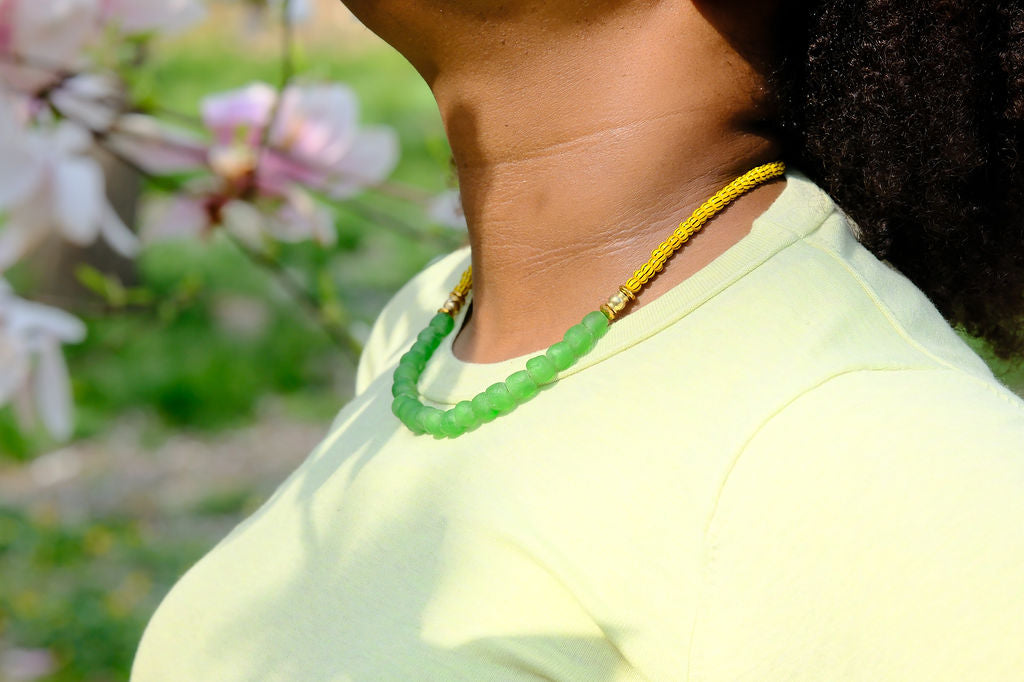 Person wearing a green necklace with a blurred floral background