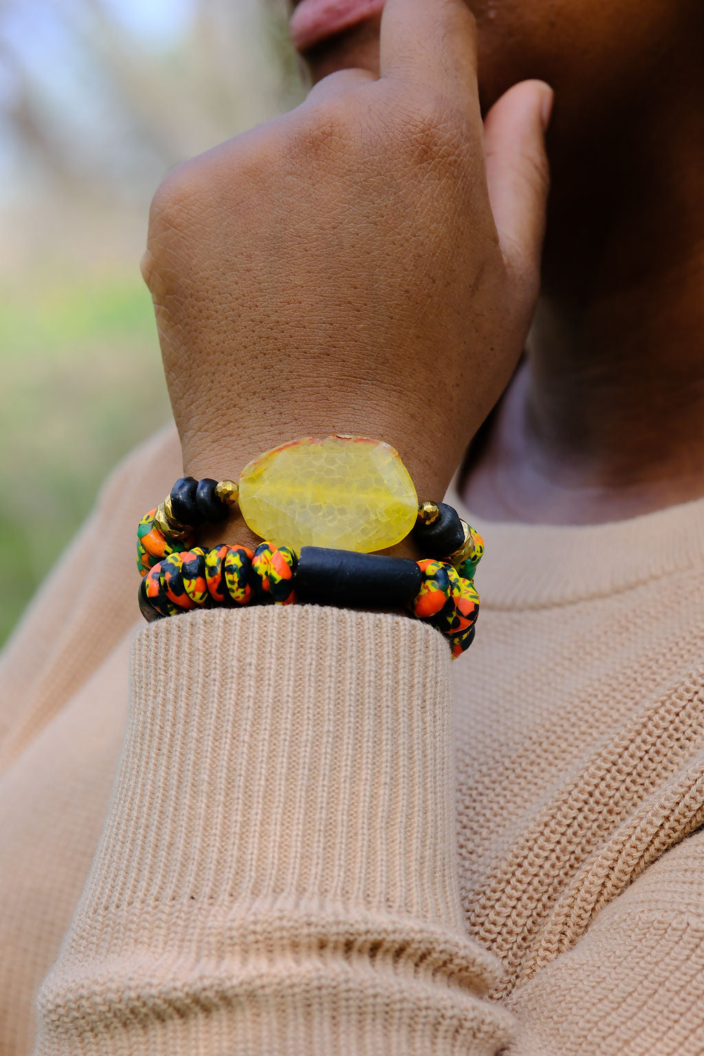 Close-up of a hand wearing a colorful beaded bracelet with a blurred natural background