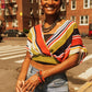 Woman wearing a colorful striped top and jeans on a city street.