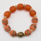 Bracelet with orange beads and gold accents on a white background