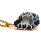 Necklace with a black and white agate pendant on a gold chain against a white background