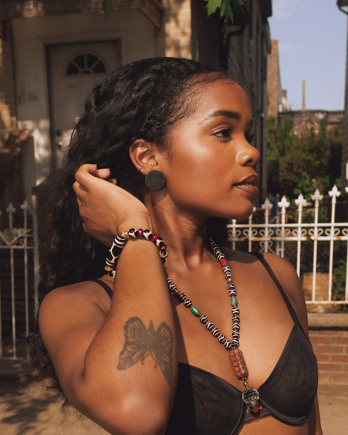 Woman wearing a black bralette with colorful beads and jewelry, outdoors.