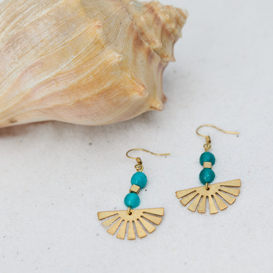 Gold earrings with turquoise beads next to a shell on a light background