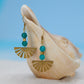 Gold earrings with turquoise beads on a seashell against a blue background