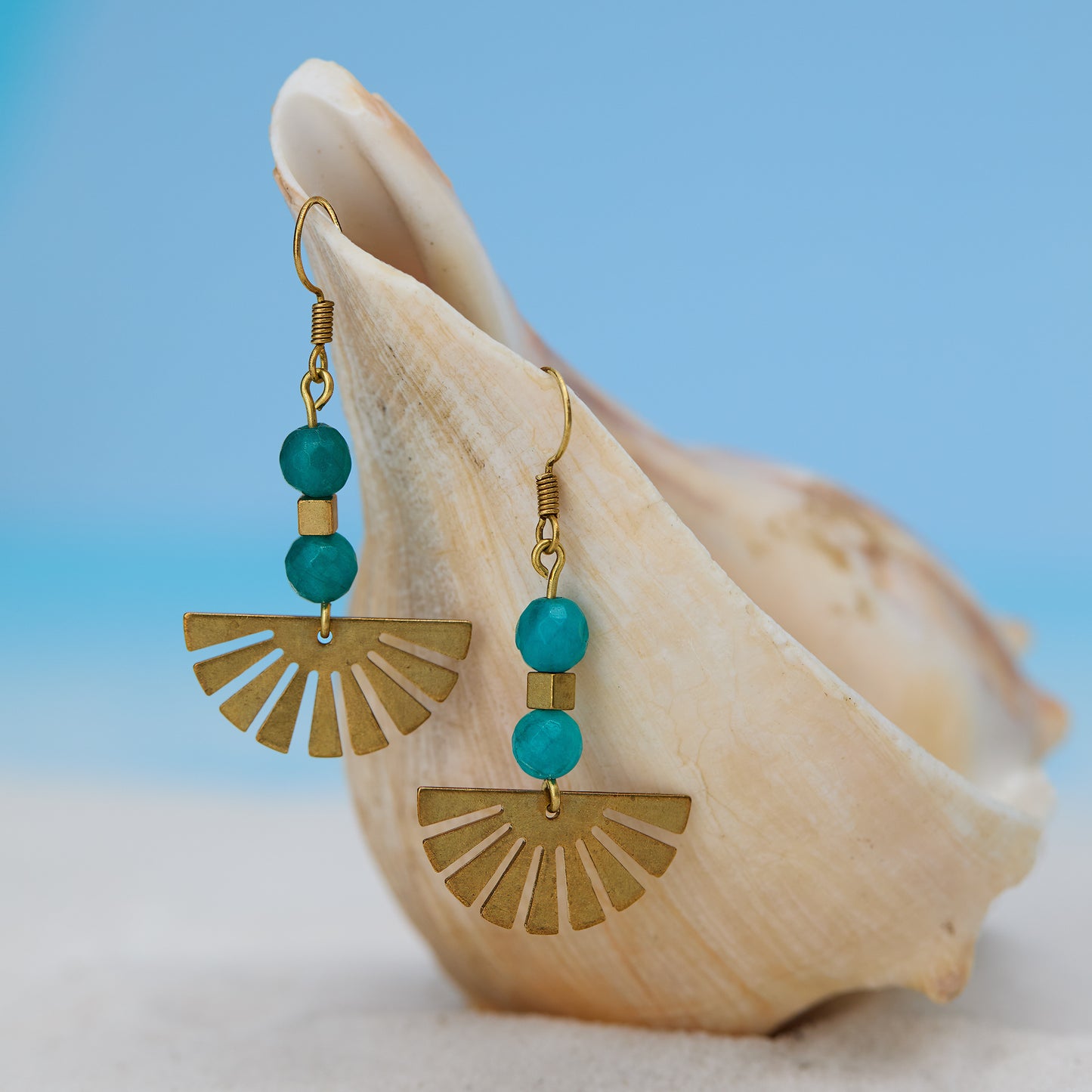 Gold earrings with turquoise beads on a seashell against a blue background