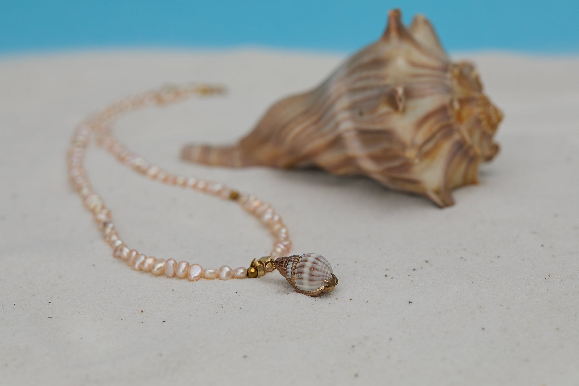 Shell necklace with a shell pendant on a sandy surface with a blue background
