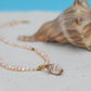 Pearl necklace with a shell pendant on a sandy surface with a shell in the background