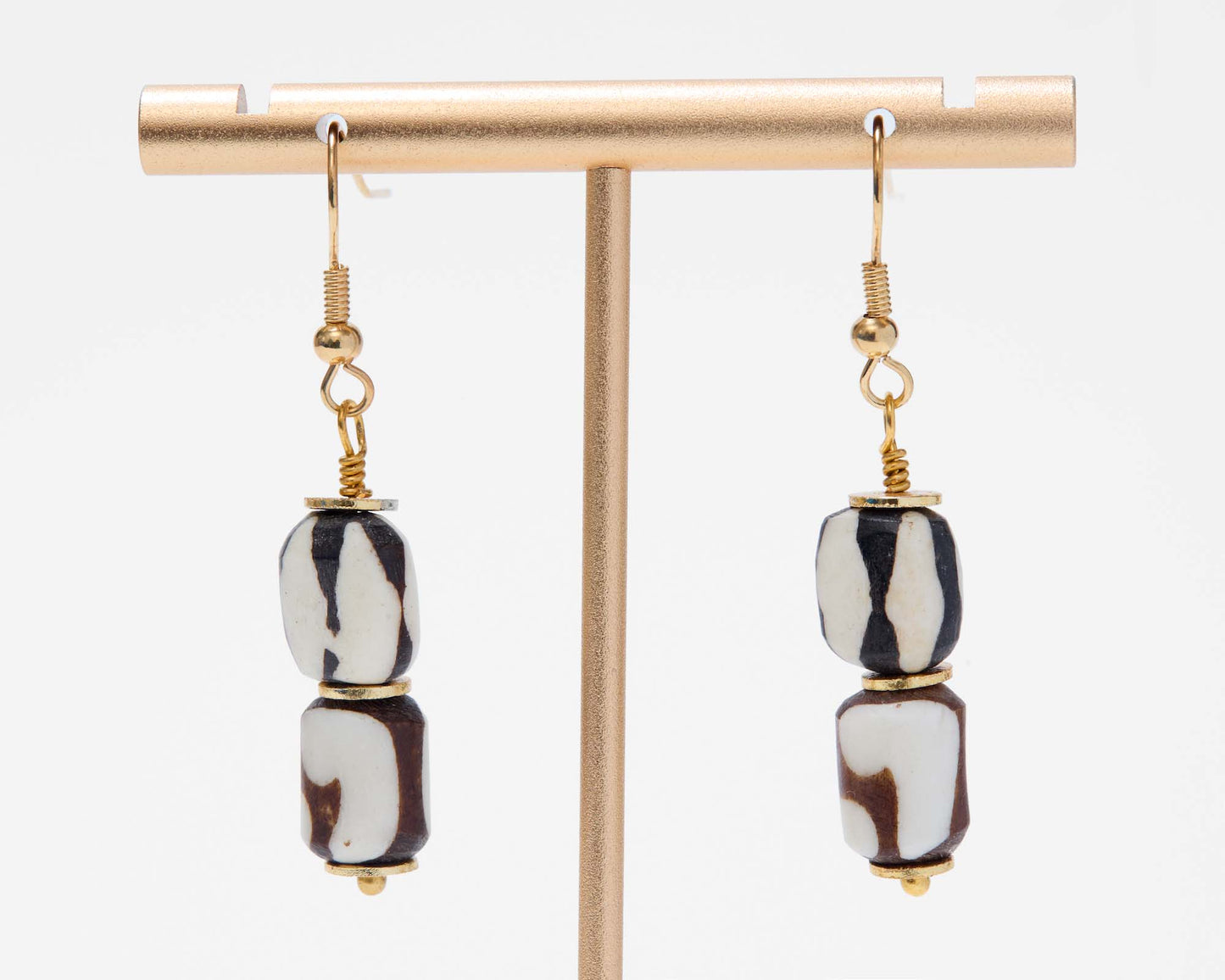 Pair of earrings with black and white beads on a gold earring stand against a white background
