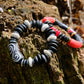 Two bracelets with black, white, and red beads on a wooden surface