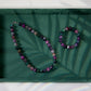Gemstone necklace and bracelet set on a green tray with leaf shadows