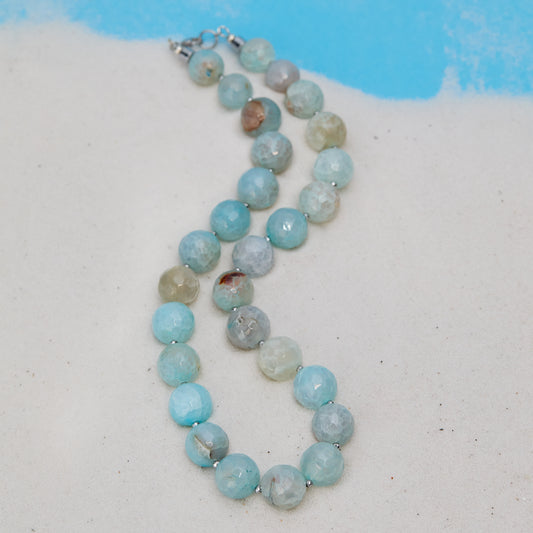 Necklace with blue beads on a sandy surface with a blue background