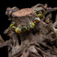 A bead bracelet with a combination of brown, black, and green faceted beads with hematite accents, on a tree stump against a black background. 