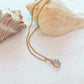 Gold necklace with a shell pendant on a sandy surface with seashells.