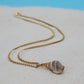 Necklace with a shell pendant on a sandy surface with a blue background