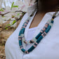 Person wearing a colorful beaded necklace with a blurred floral background