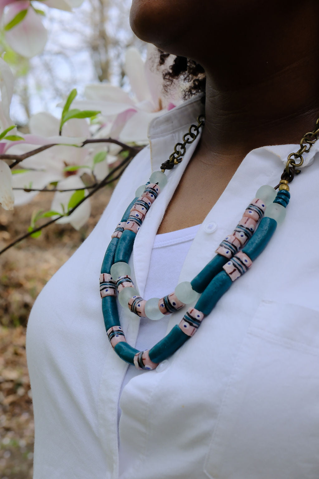 Person wearing a colorful beaded necklace with a blurred floral background