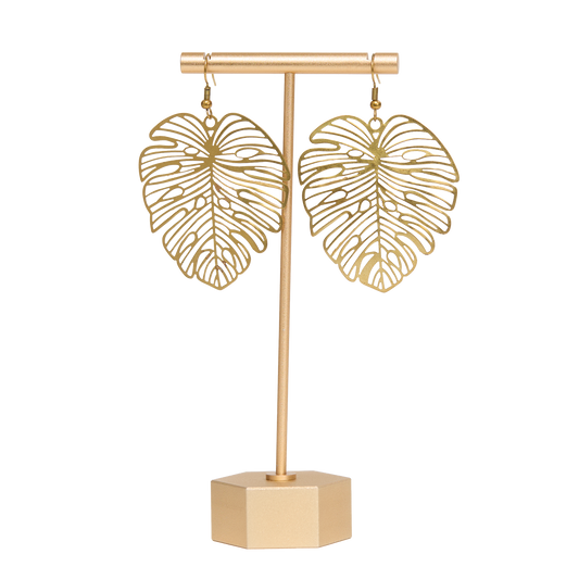 Brass monstera leaf-shaped earrings on a matching stand with a white background