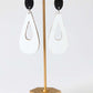 Gold earring stand with teardrop-shaped earrings on a white background