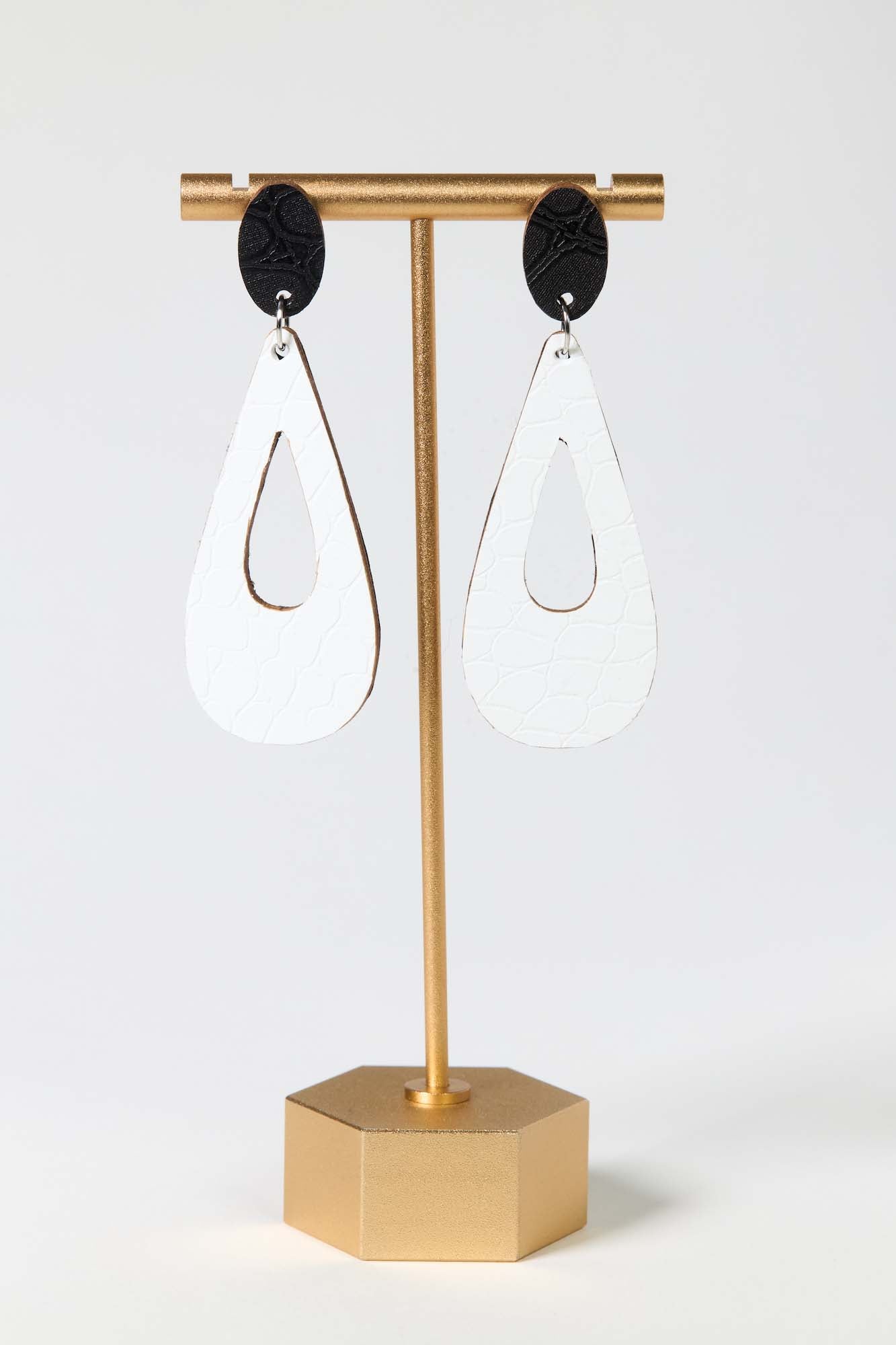 Gold earring stand with teardrop-shaped earrings on a white background