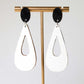 White teardrop earrings with black accents on a gold earring stand against a white background