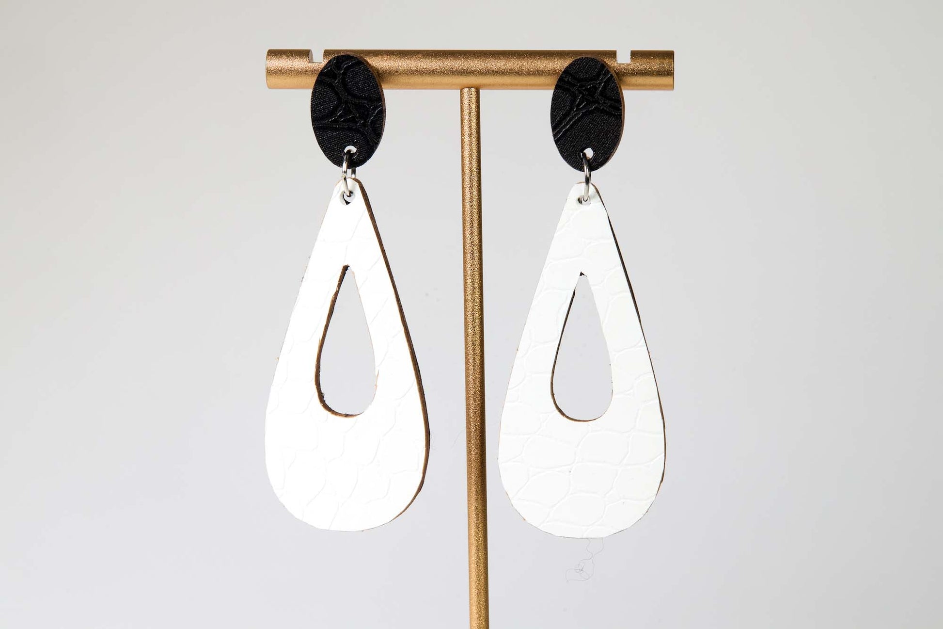 White teardrop earrings with black accents on a gold earring stand against a white background