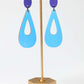 Blue earrings on a gold stand against a white background
