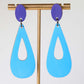 Blue teardrop earrings with purple accents on a stand against a white background
