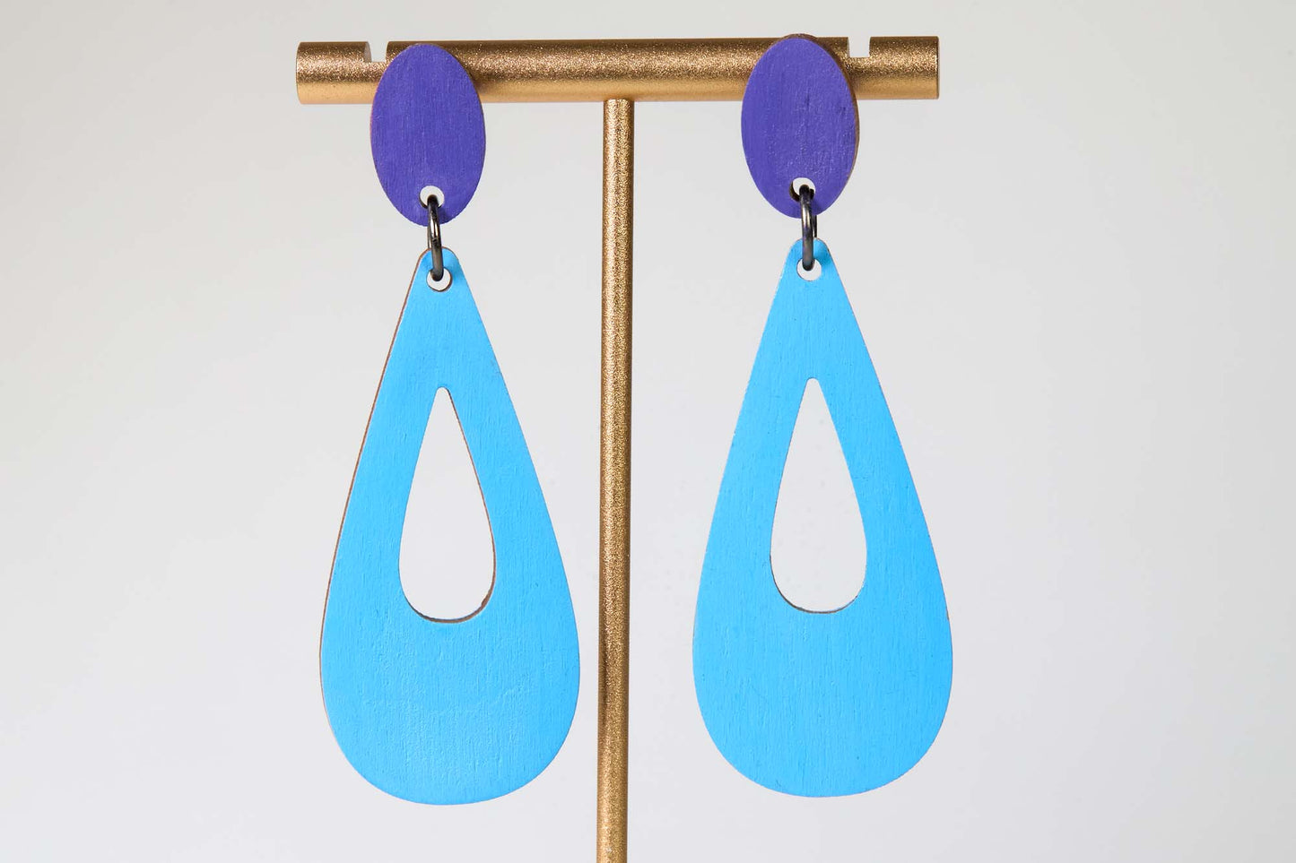 Blue teardrop earrings with purple accents on a stand against a white background