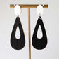 Black teardrop earrings on a gold earring stand against a white background